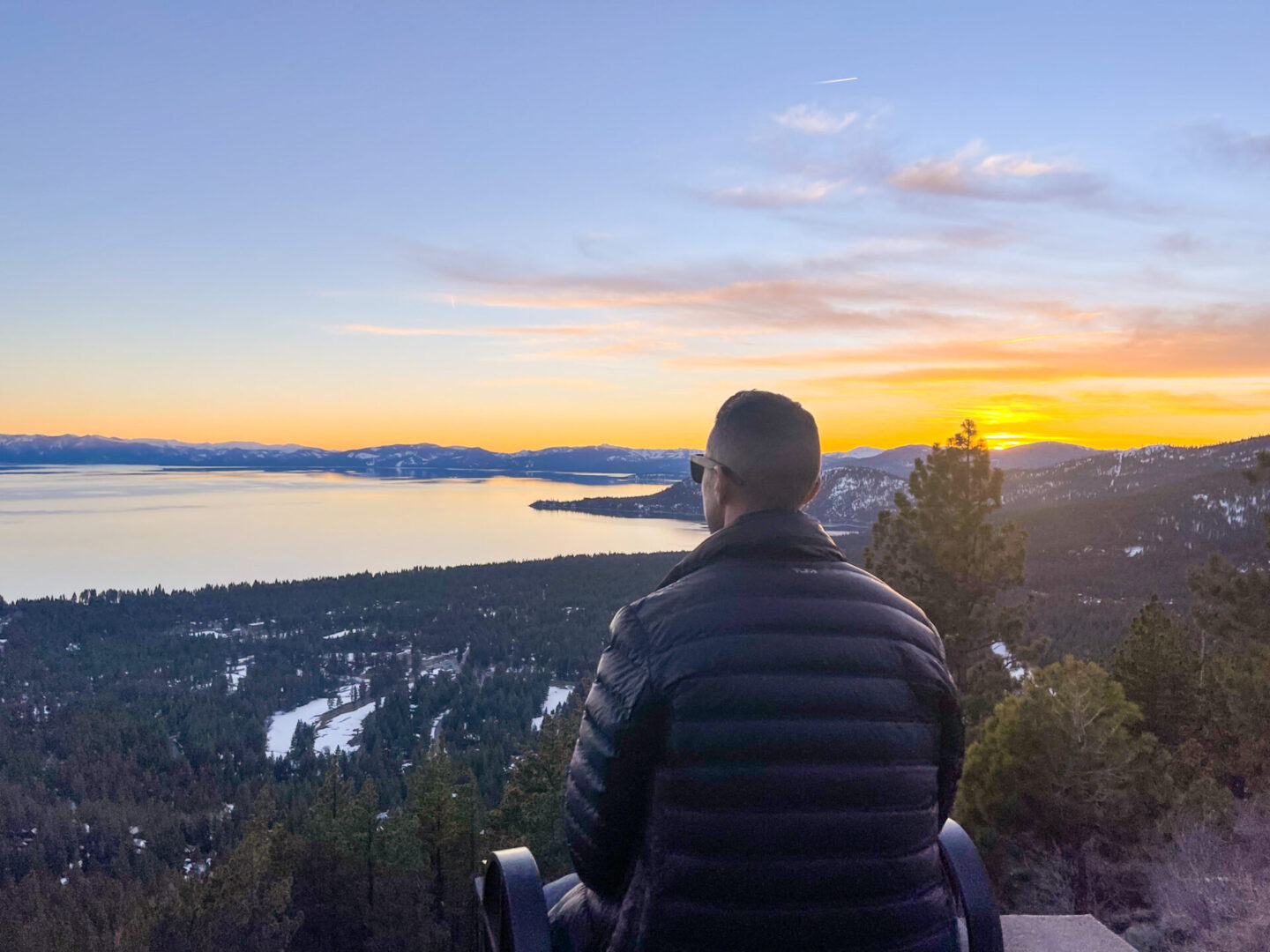 A man standing on top of a mountain looking at the sunset.