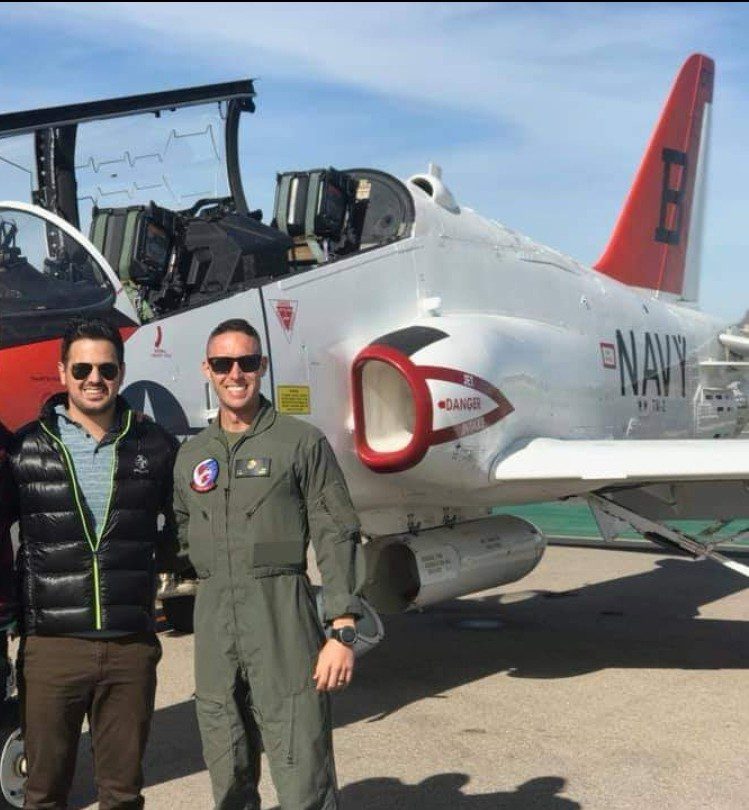 Two men standing in front of a fighter jet.